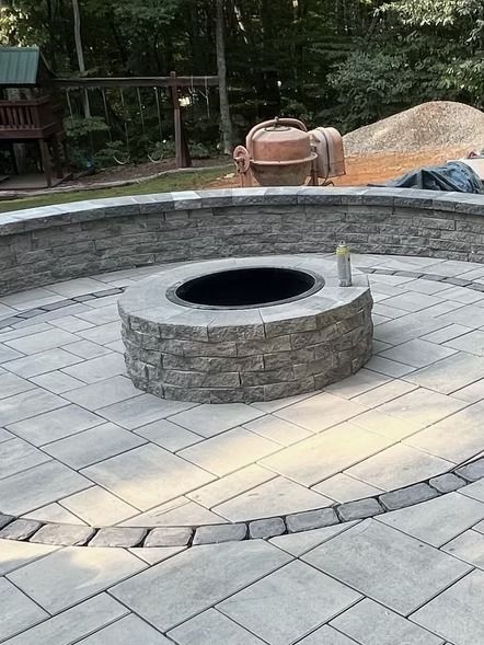Stone fire pit in a paved courtyard with a circular seating wall and surrounding outdoor landscaping