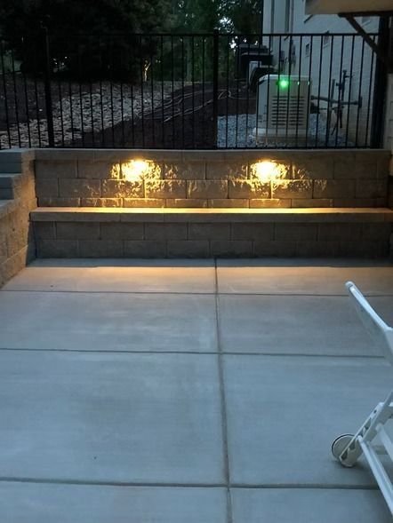 Backyard patio with lit stone bench wall and metal gate at dusk