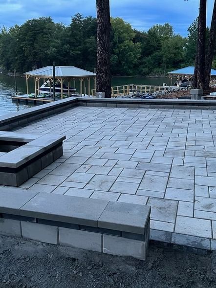 Raised stone patio under construction beside a lakeside dock and trees