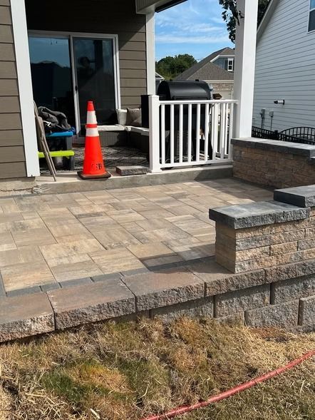 Stone patio with steps and white railing beside a house; orange traffic cone near the doorway.