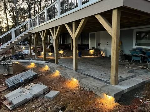 Elevated wooden deck with stairs and warm ground lights beside a patio under construction