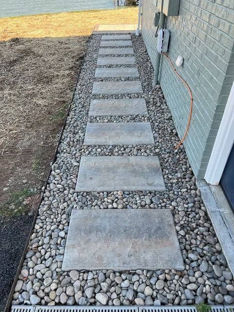 Stepping stone path through gravel beside a house, leading toward a grassy yard.