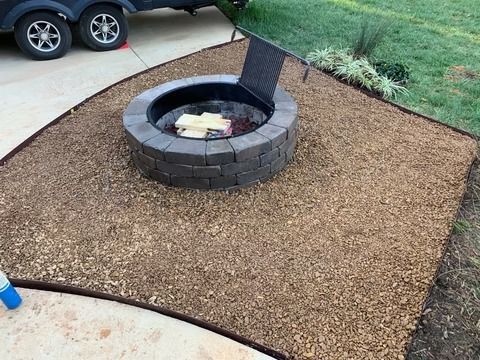 Backyard fire pit with black chimney on a gravel patio beside a driveway.