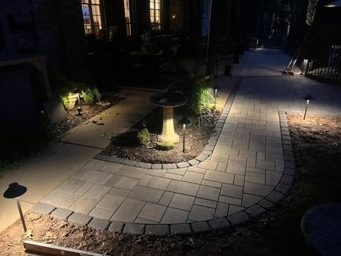 Illuminated curved stone walkway in a dark garden at night, with small path lights and plants