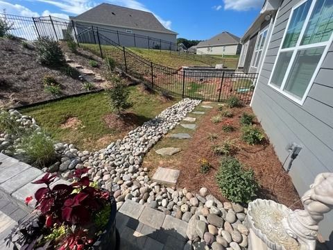 Backyard garden bed with stone border, red plants, and a house wall on the right