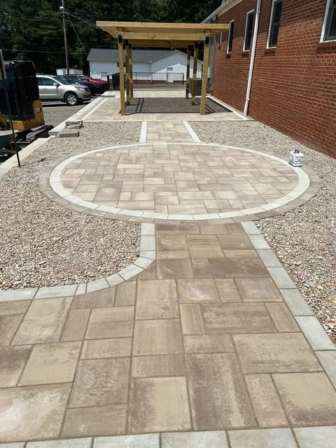 Accessible paved walkway with circular patio leading to a wooden pergola beside a brick building