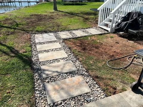 Stepping stone path bordered by pebbles leading to a white porch by the water