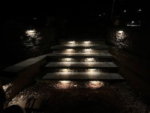 Illuminated stone steps at night beside water, with reflections on wet ground