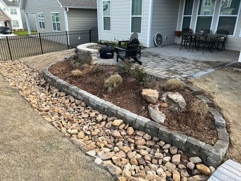 Stone-bordered front yard garden with mulch, rocks, and a patio beside a house