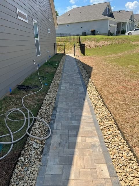 Narrow brick walkway beside a house, with gravel edging and a coiled hose on the grass.