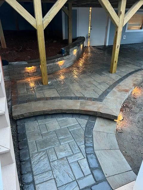 Curved stone patio steps and walkway beside a pool with wooden posts and warm lights