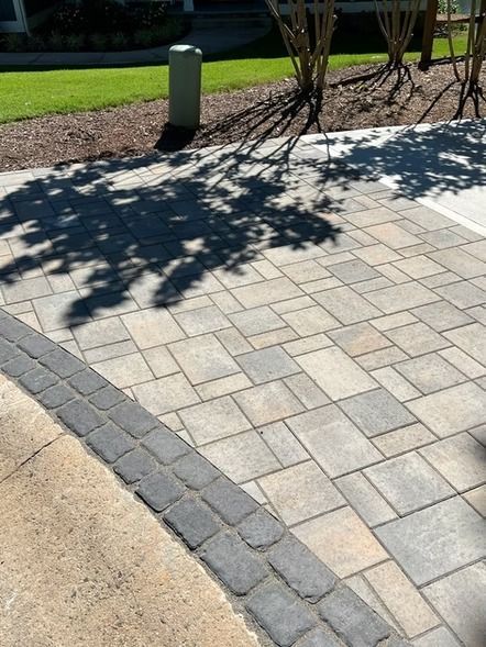 Paved walkway with gray pavers and a curved border beside grass, with tree shadows across the path.
