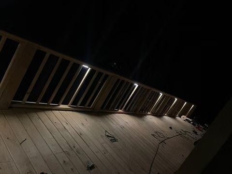 Dimly lit wooden railing along a slanted deck at night with distant lights