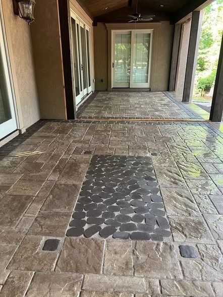 Covered walkway with stone pavers and a dark tactile strip leading to glass doors