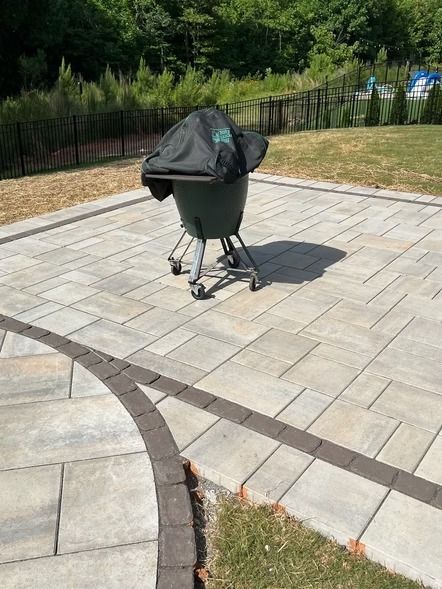Covered grill on a paved patio near grass and a black fence
