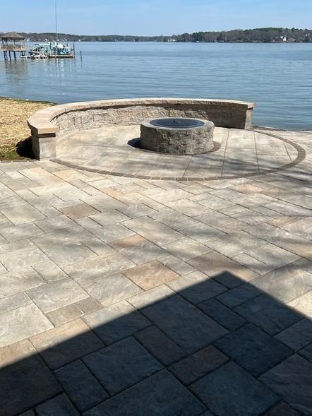 Stone patio with a curved bench and fire pit overlooking a calm lake on a sunny day