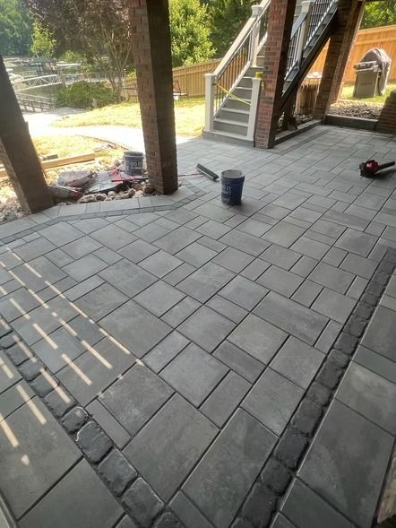 Covered patio with gray paver flooring, stairs, brick columns, and a bucket in the center.