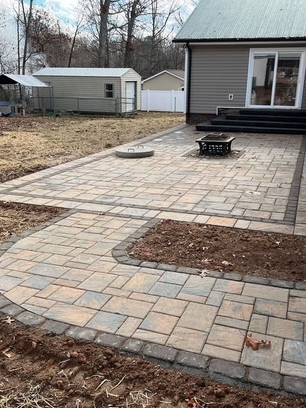 Backyard patio with stone pavers, raised fire pit, and a house in the background