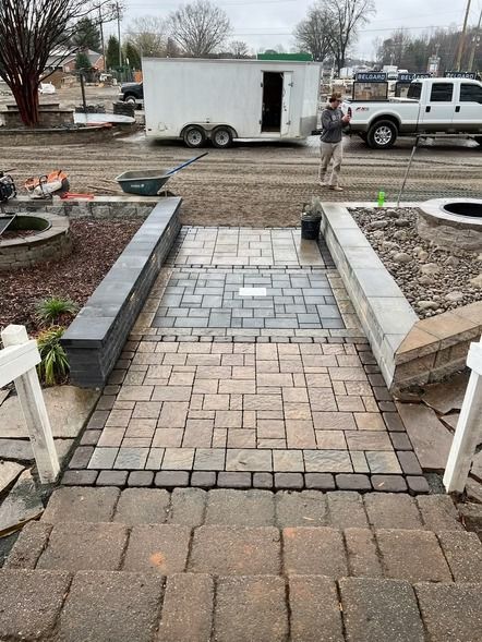 Stone walkway under construction with pavers, edging, and a worker near a trailer in the background
