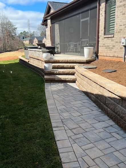 Backyard patio with stone steps, paved walkway, grass lawn, and house exterior on a sunny day