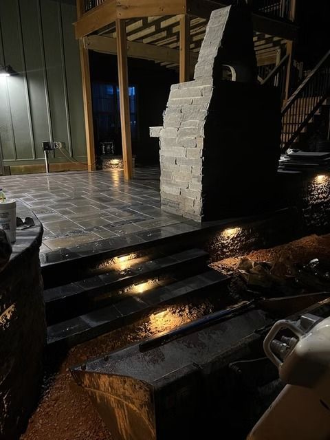 Rainy nighttime patio with wet dark steps, stone column, and tiled floor reflecting light