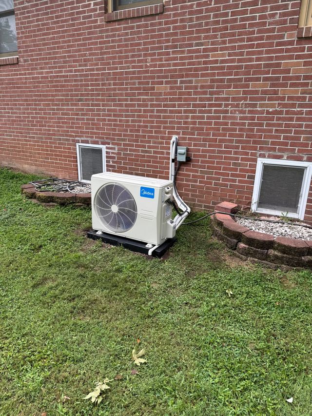 Outdoor HVAC unit beside a brick house wall on a grassy lawn
