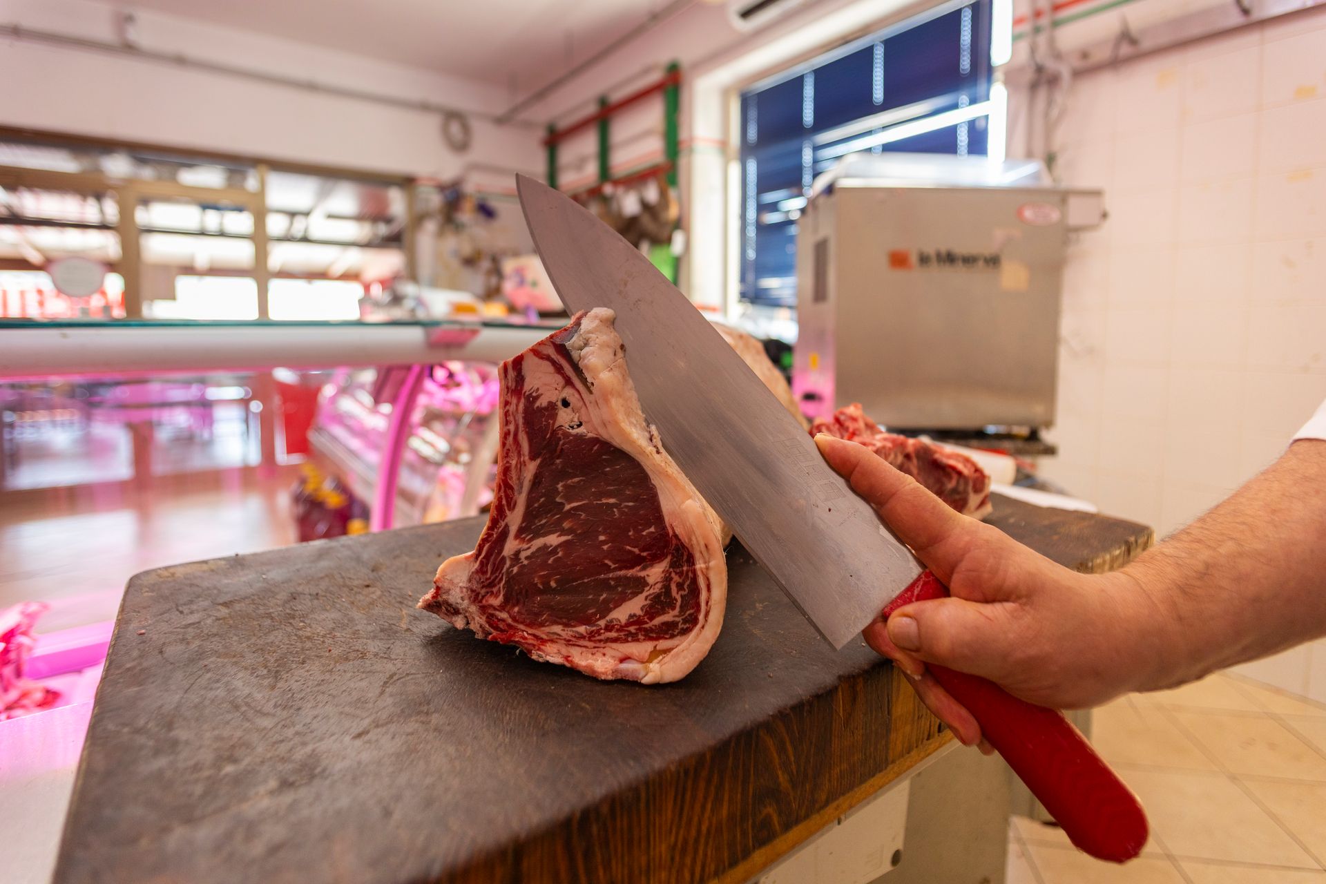 Un macellaio affetta una bistecca di costata cruda su un tagliere in una macelleria.