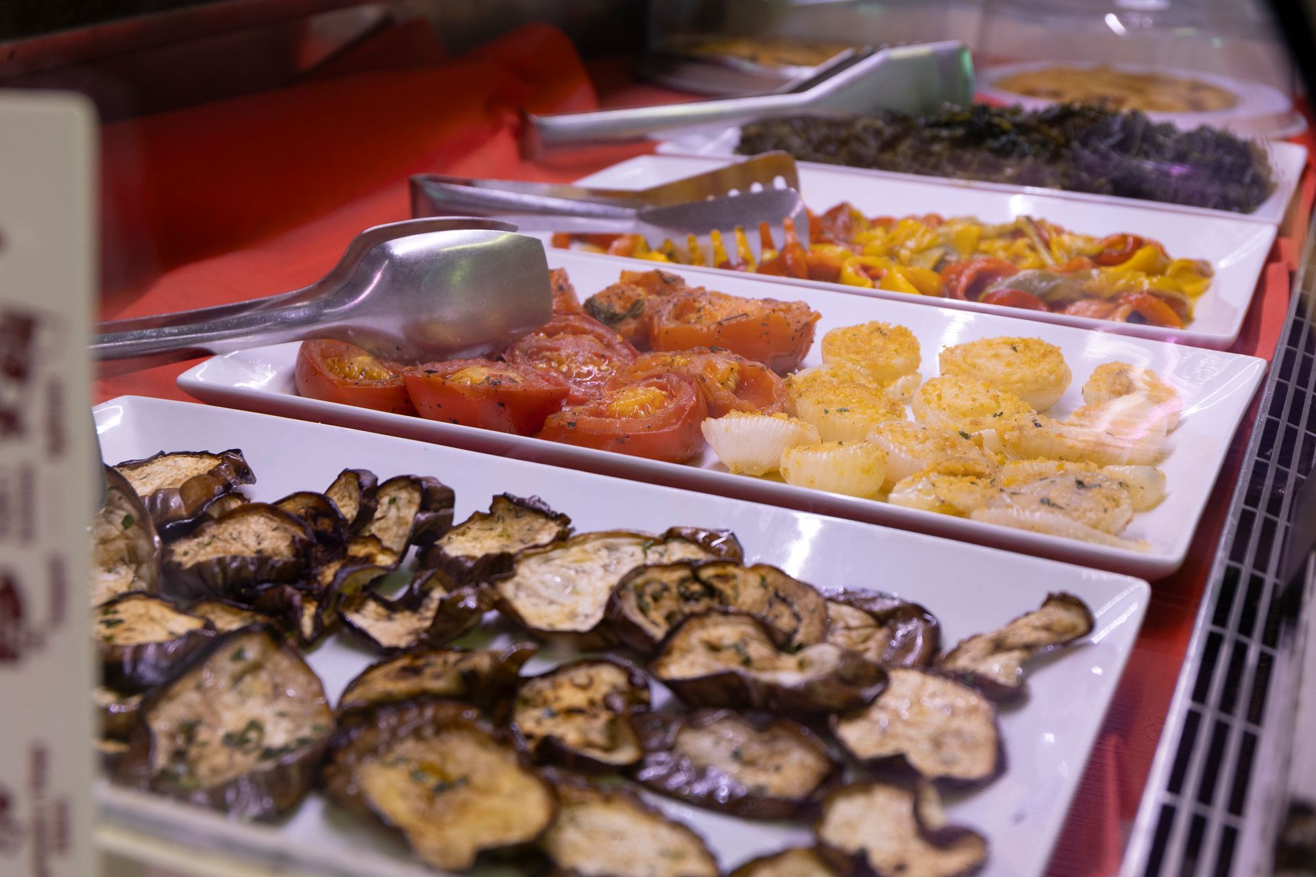 Vassoi da buffet con verdure arrosto assortite e altri piatti su un bancone di servizio.