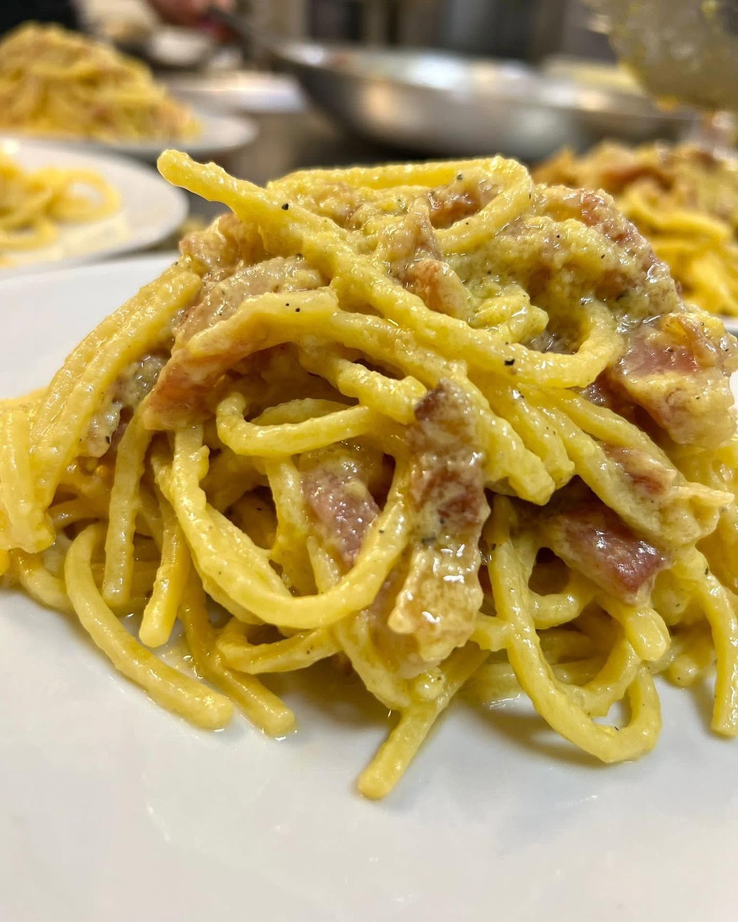 Piatto di spaghetti alla carbonara con cremosa salsa gialla e pezzetti di pancetta in un piatto bianco.