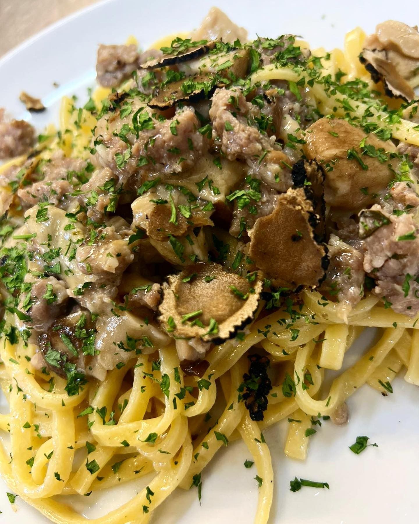 Pasta condita con un cremoso ragù di carne, erbe aromatiche e scaglie di tartufo, servita su un piatto bianco.