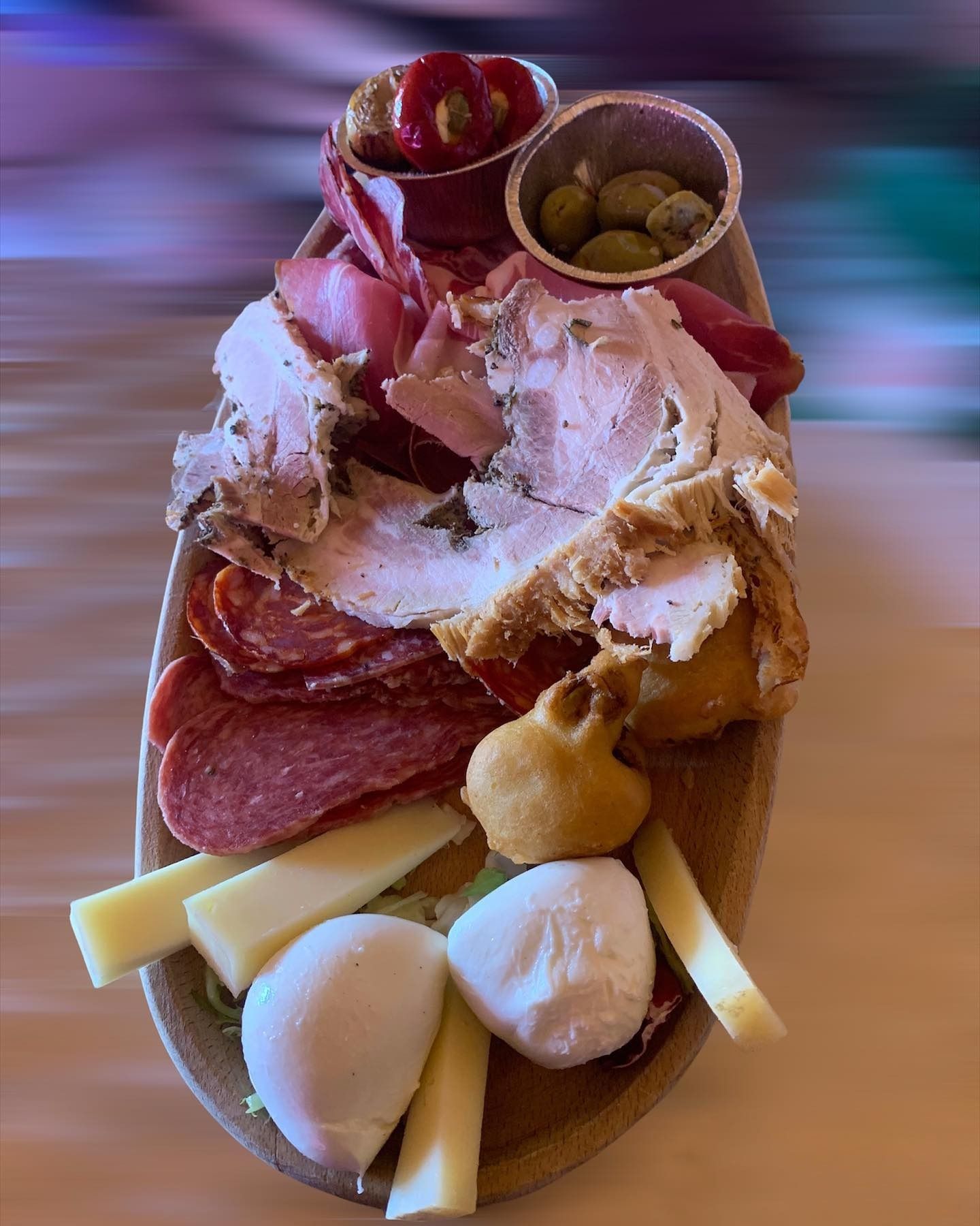 Tagliere di salumi con salame, formaggio, prosciutto, uva e olive su una paletta di legno.