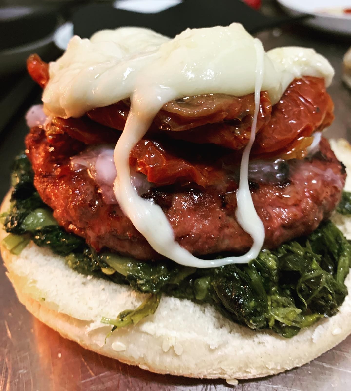 Un hamburger a strati con formaggio fuso, pomodoro, verdure e salsa in un panino.