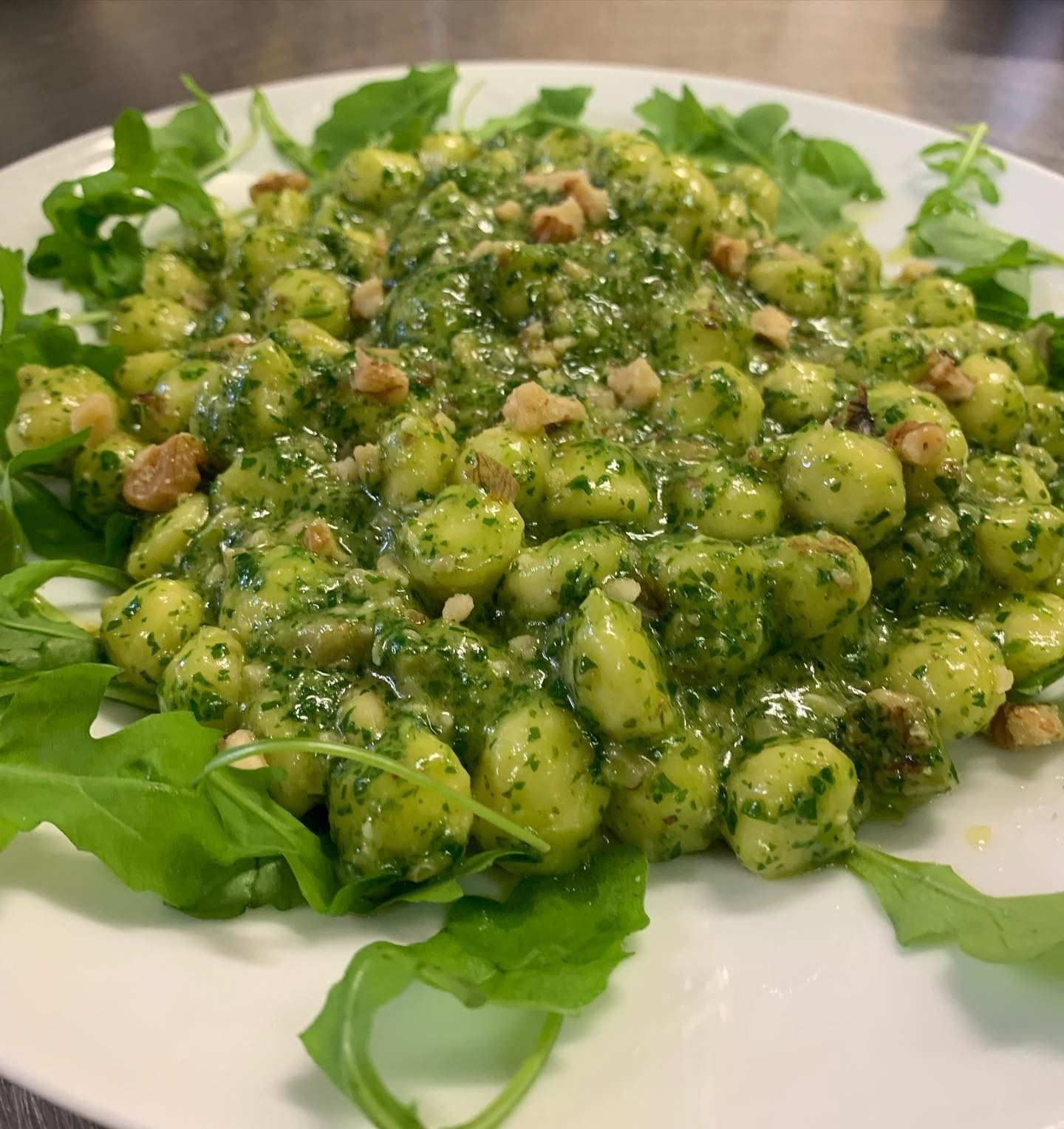 Gnocchi al pesto verde con formaggio e crostini, serviti su un piatto bianco foderato di rucola.