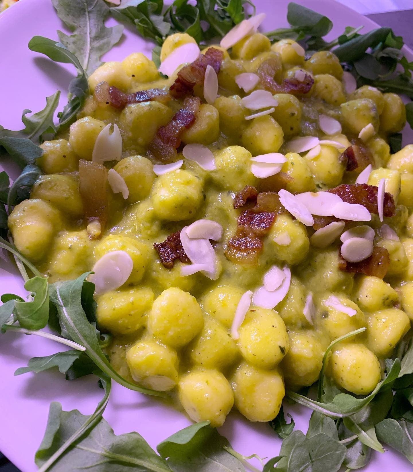 Curry di ceci gialli guarnito con mandorle a lamelle ed erbe aromatiche, servito in una ciotola.