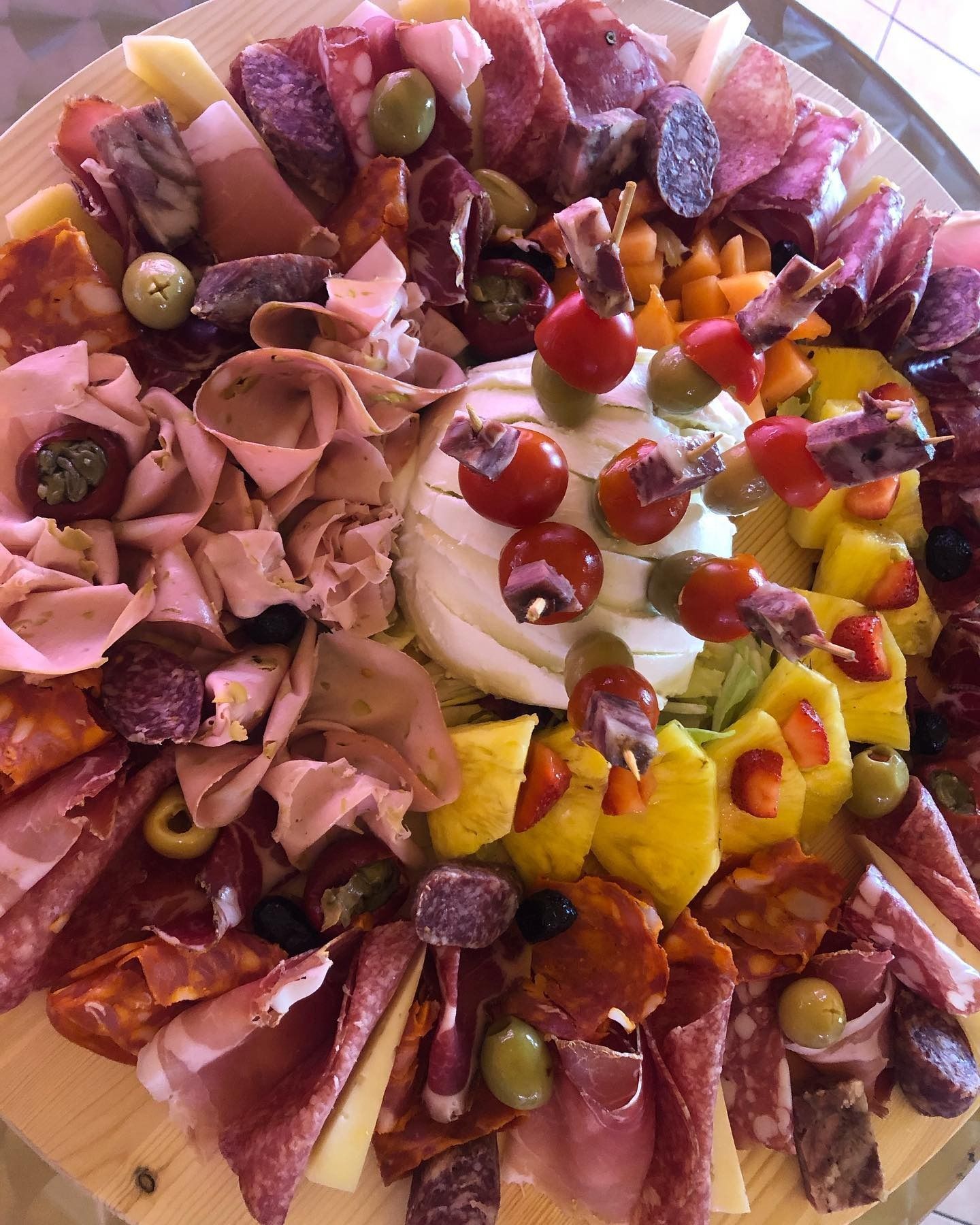 Affettati assortiti, formaggi, olive, peperoni e pomodorini disposti su un piatto rotondo