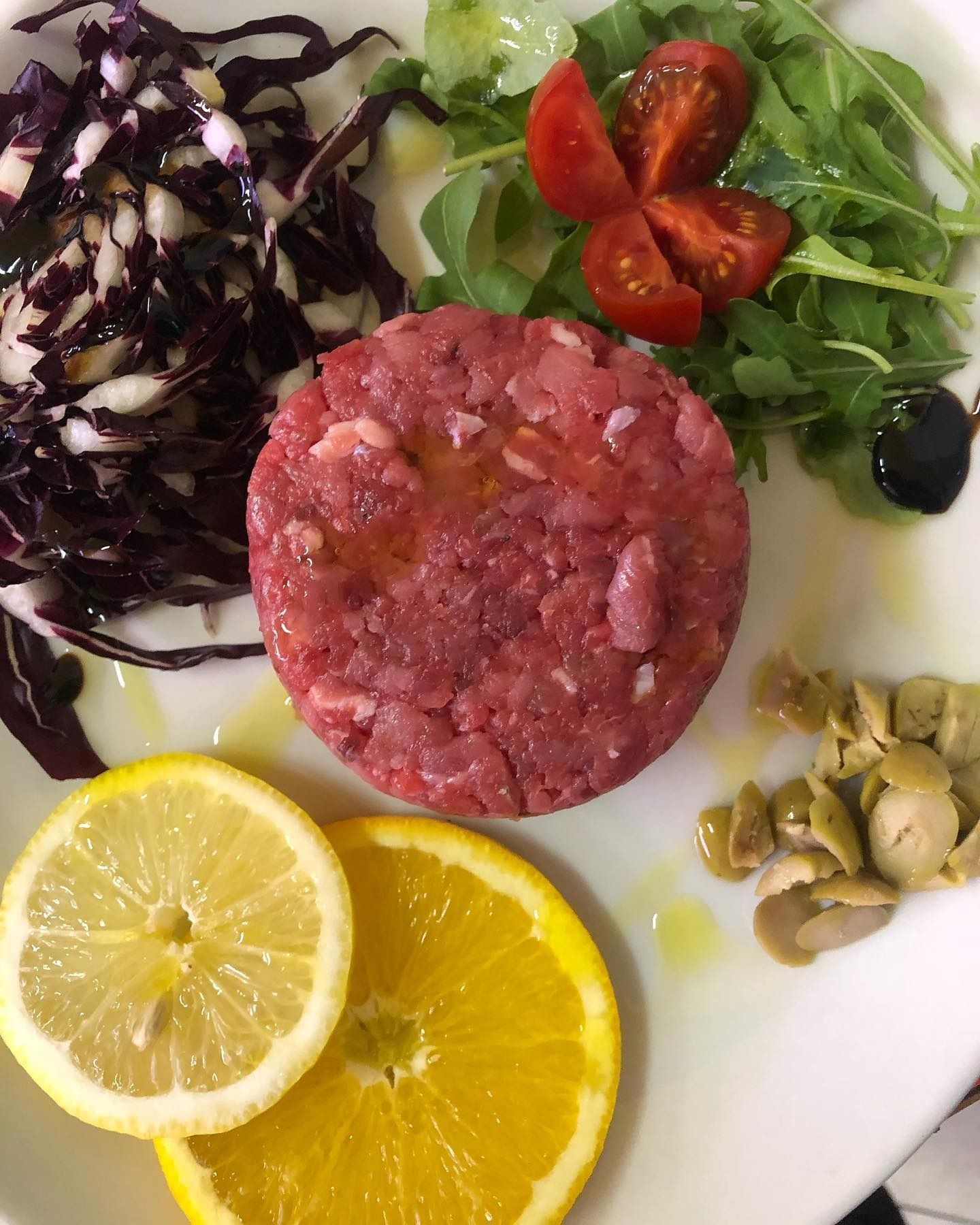 Piatto di carne macinata cruda con fette di limone, pomodorini, verdure, olive e insalata di cavolo.