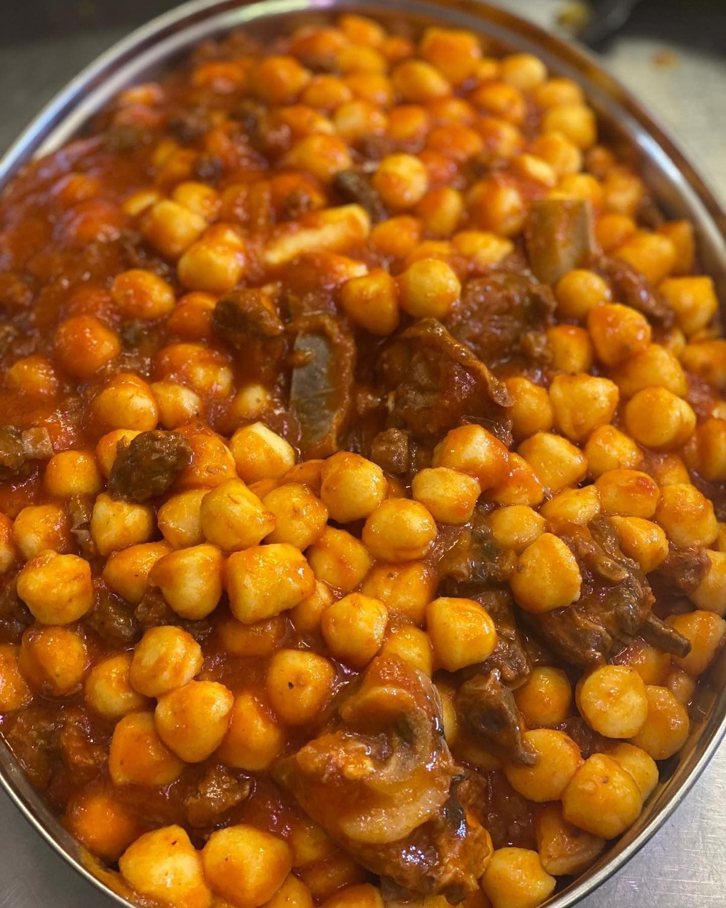 Ciotola di curry di ceci con fagioli dorati e lucenti e salsa rosso-marrone scuro.