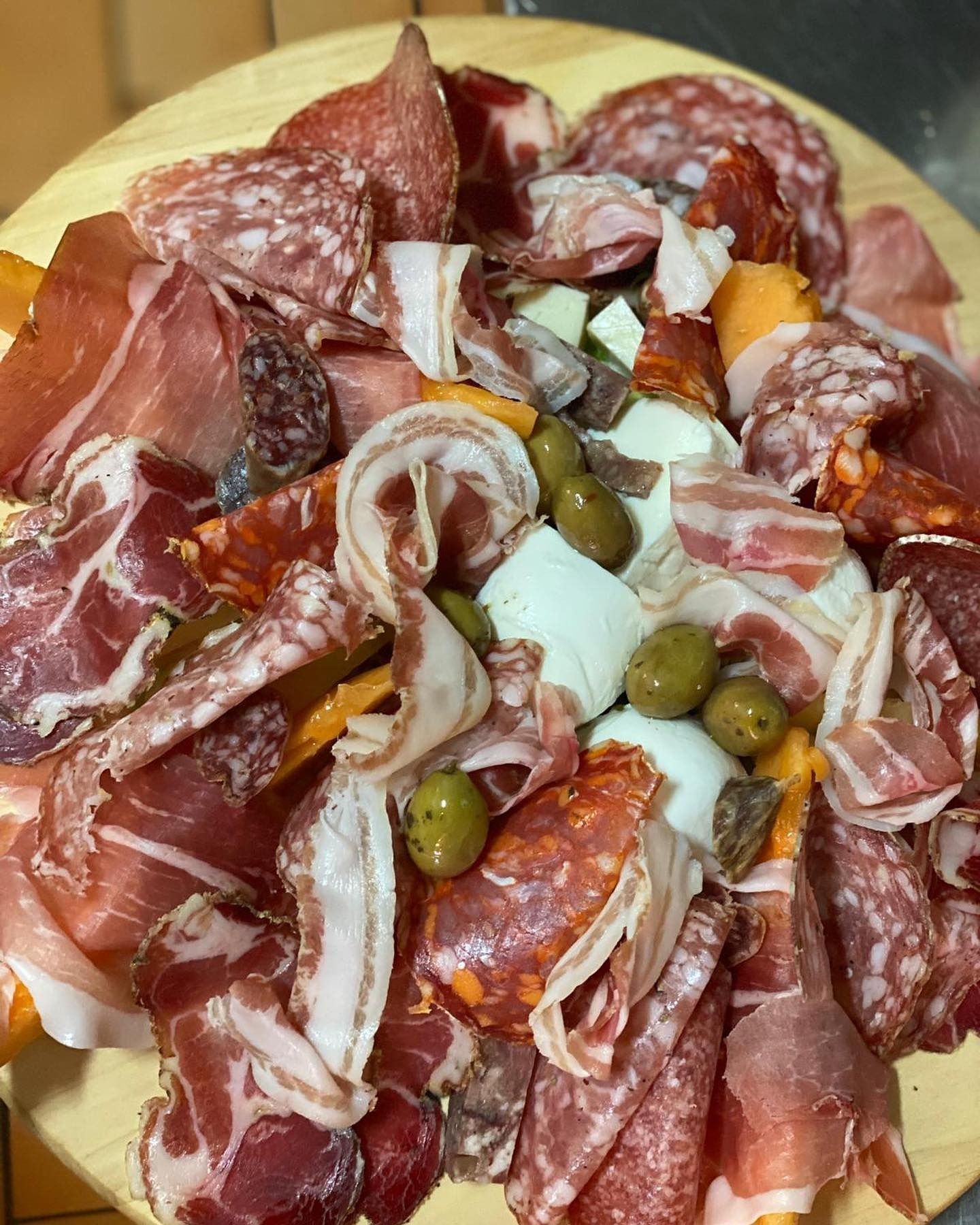 Piatto di salumi assortiti e olive verdi su un tagliere di legno.