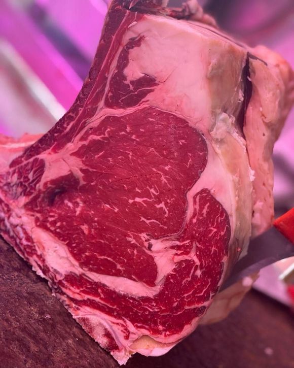 Primo piano di una bistecca cruda marmorizzata con l'osso, illuminata da una luce rosa-violacea.