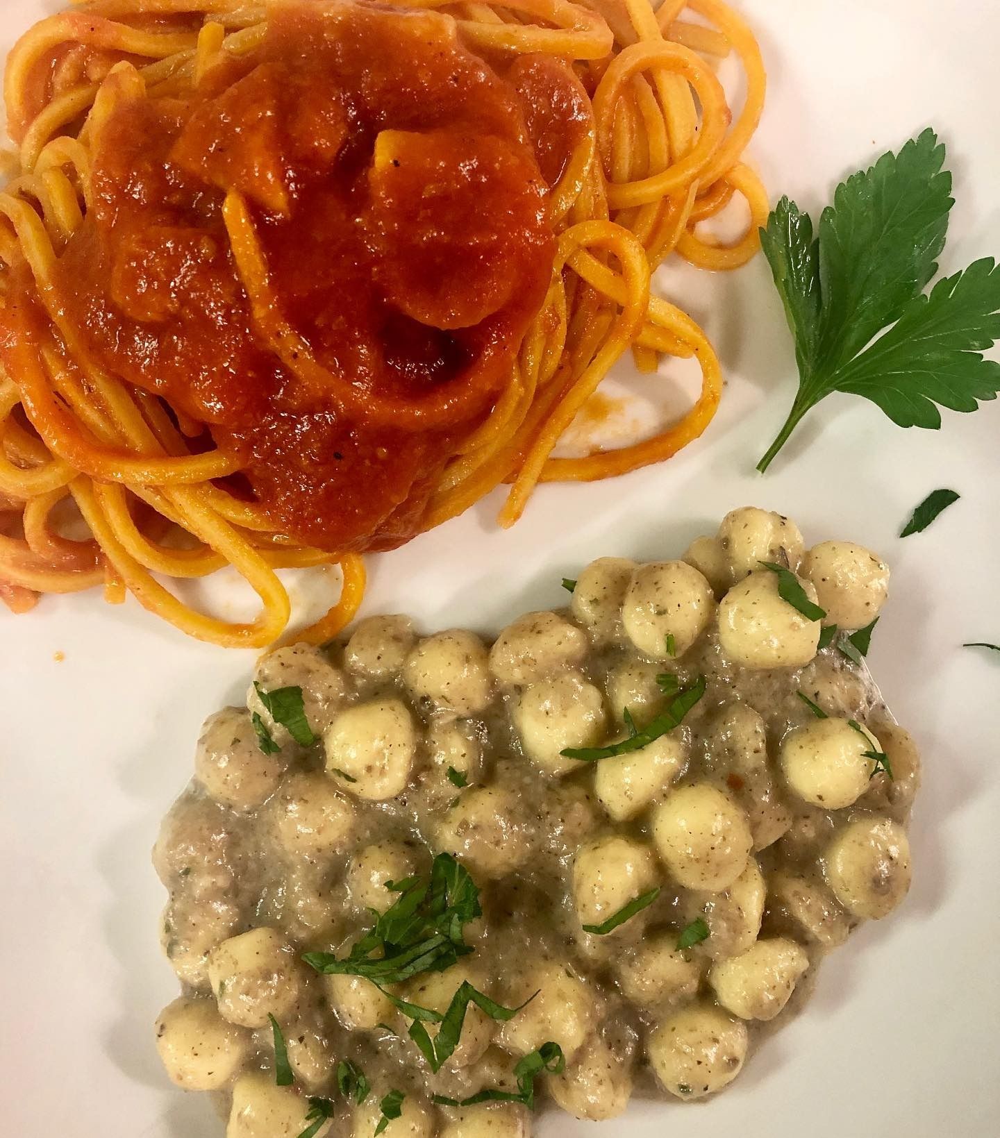 Spaghetti al sugo di pomodoro e un piatto di gnocchi cremosi guarniti con prezzemolo su un piatto bianco.