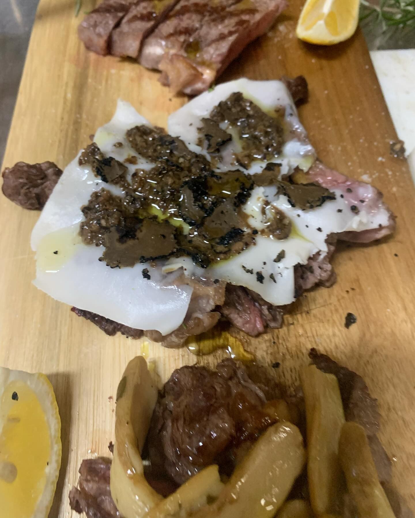 Bistecca alla griglia con formaggio fuso e pepe, servita su un tagliere di legno, con patatine fritte e uno spicchio di limone.