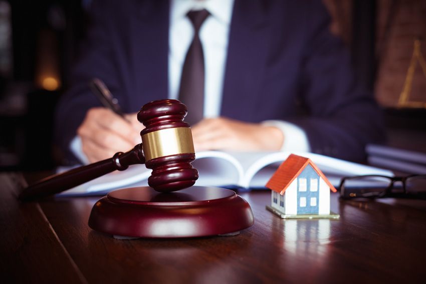 A Man is Sitting at a Table With a Gavel and a Small House — Budd & Piper Solicitors & Conveyancers in Tweed Heads, NSW