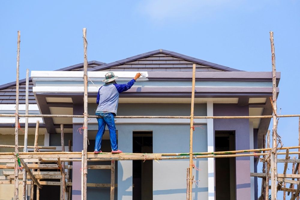 A Man is Standing on a Scaffolding Painting a House — Shields Painting & Decorating in Narrandera, NSW