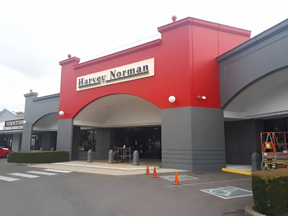 A Man is Spraying Paint on the Side of a Building — Shields Painting & Decorating in Wagga Wagga, NSW