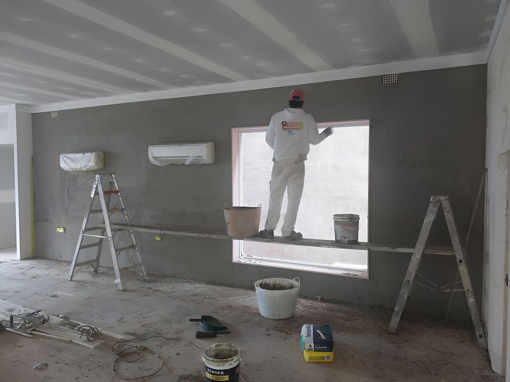 A Man is Standing on a Ladder Painting a Wall — Shields Painting & Decorating in Temora, NSW