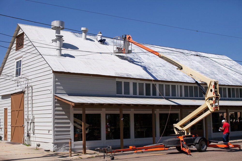 A Man is Painting the Roof of a Building With a Crane — Shields Painting & Decorating in Temora, NSW