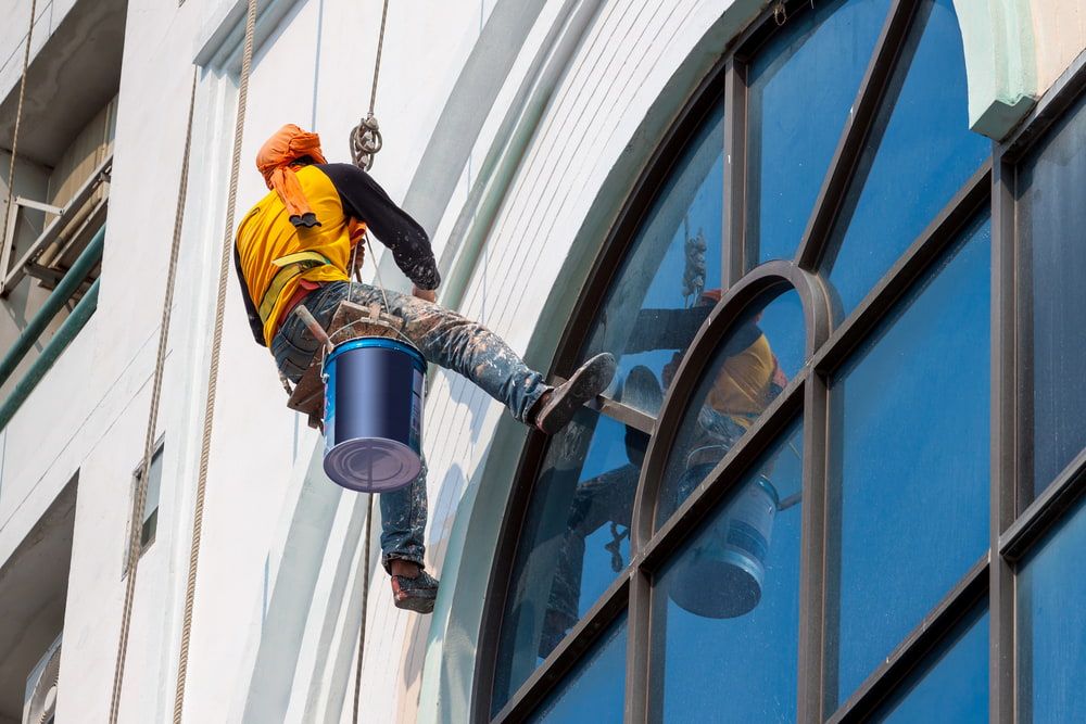 A Man is Painting the Side of a Building With a Bucket — Shields Painting & Decorating in Gundagai, NSW