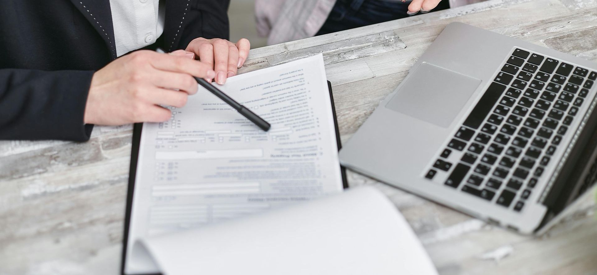 Hands holding a pen over a document with a laptop, likely in a meeting.