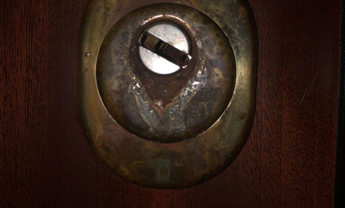 Primo piano di una serratura in ottone usurata su legno scuro, con una chiave parzialmente inserita.