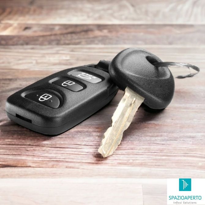 Telecomando per auto e chiave metallica su una superficie di legno, con una seconda chiave sfocata sullo sfondo.
